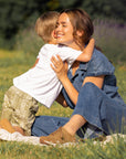 A child hugging a woman in a denim outfit and brown sneakers.