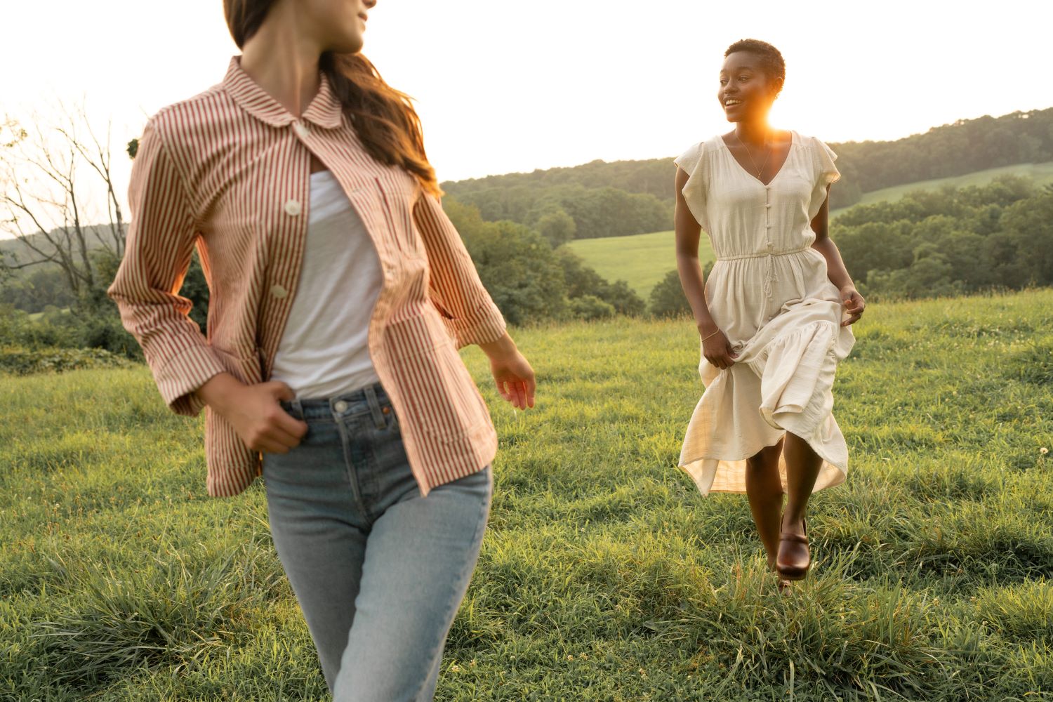 Girl in brown clogs and a white dress walking through a meadow at sunset.