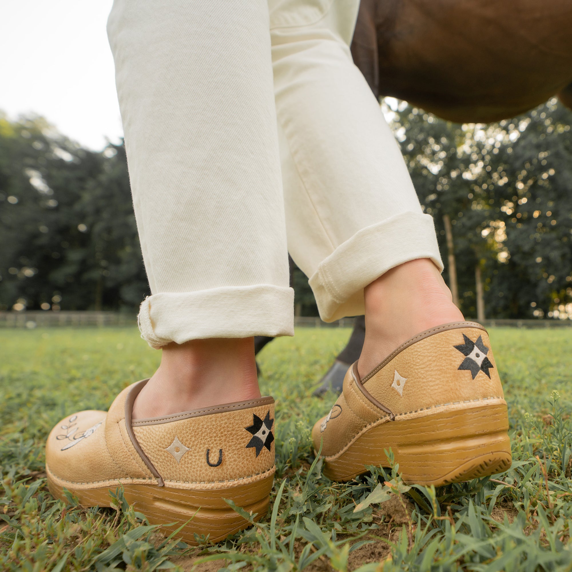 Tan clogs with star designs worn on grass
