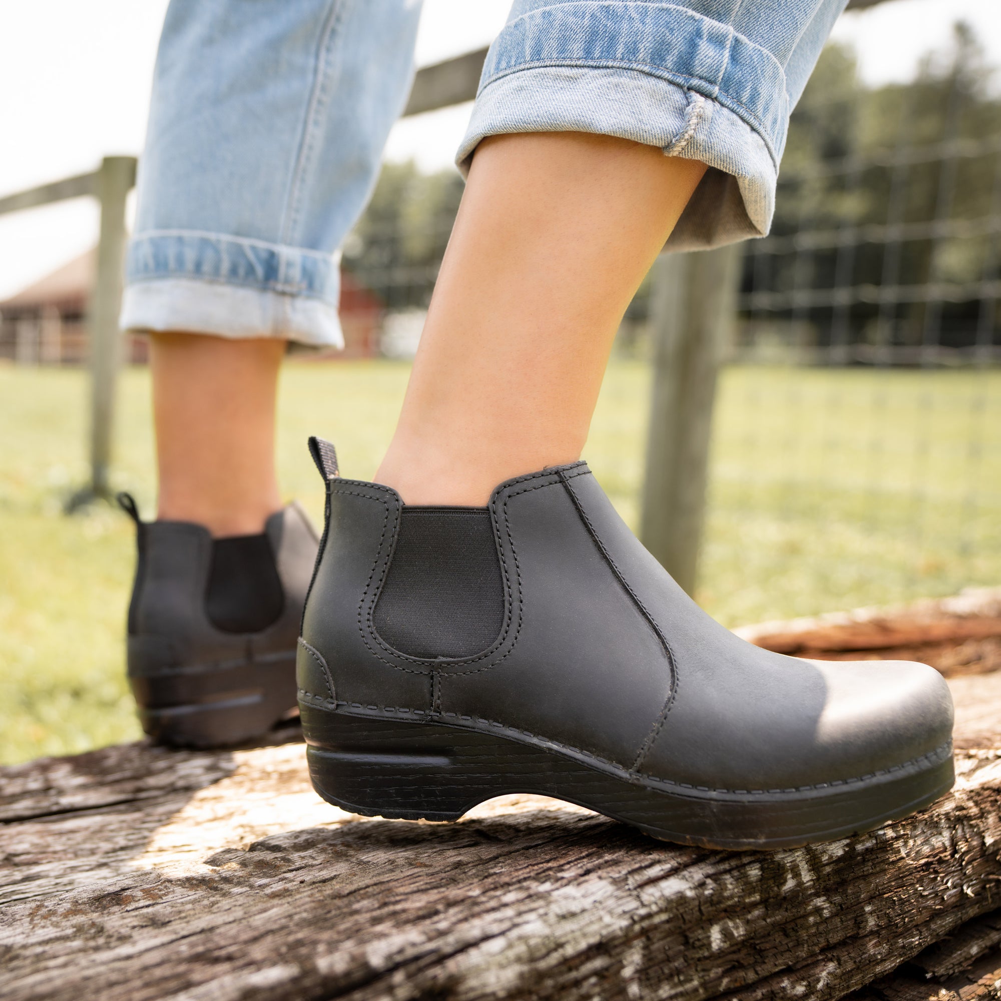 Black boots shown with light denim on a wooden plank.