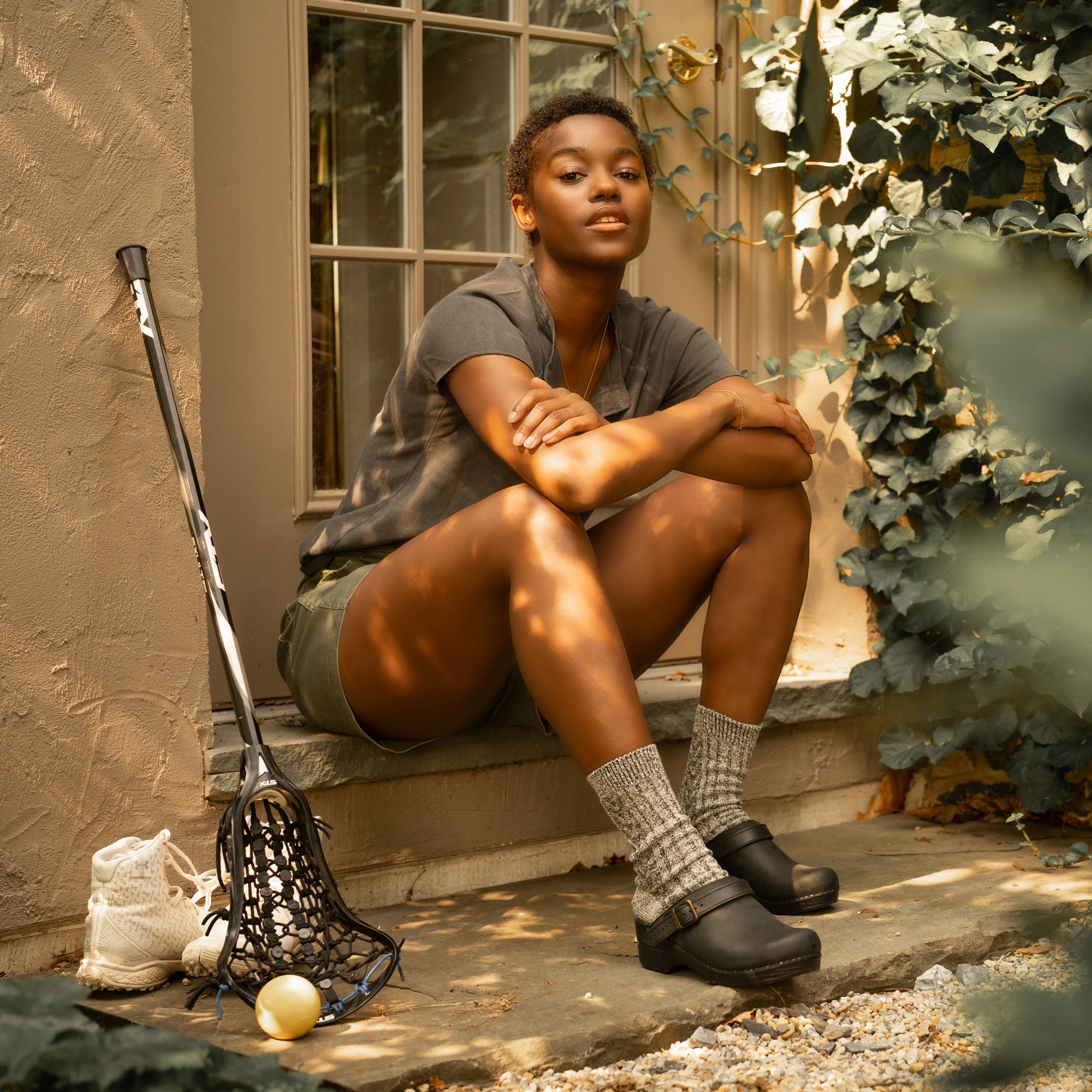 A woman sitting while wearing black backless clogs and casual clothes.
