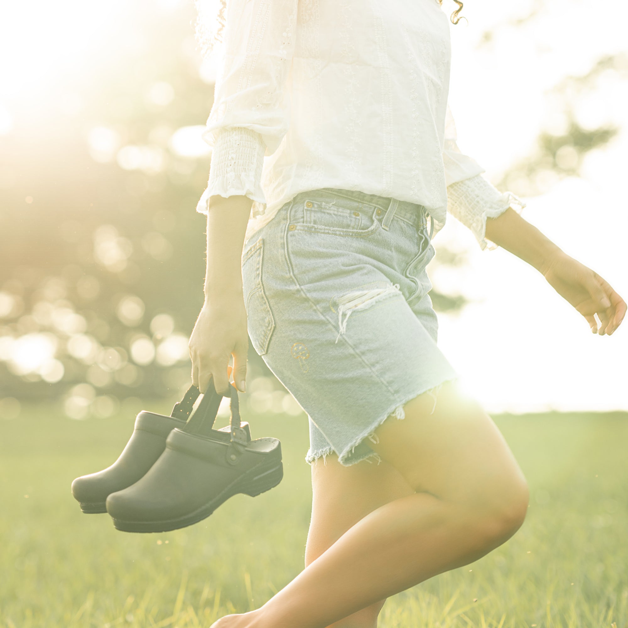 Brown swivel strap clogs held while walking through a meadow.