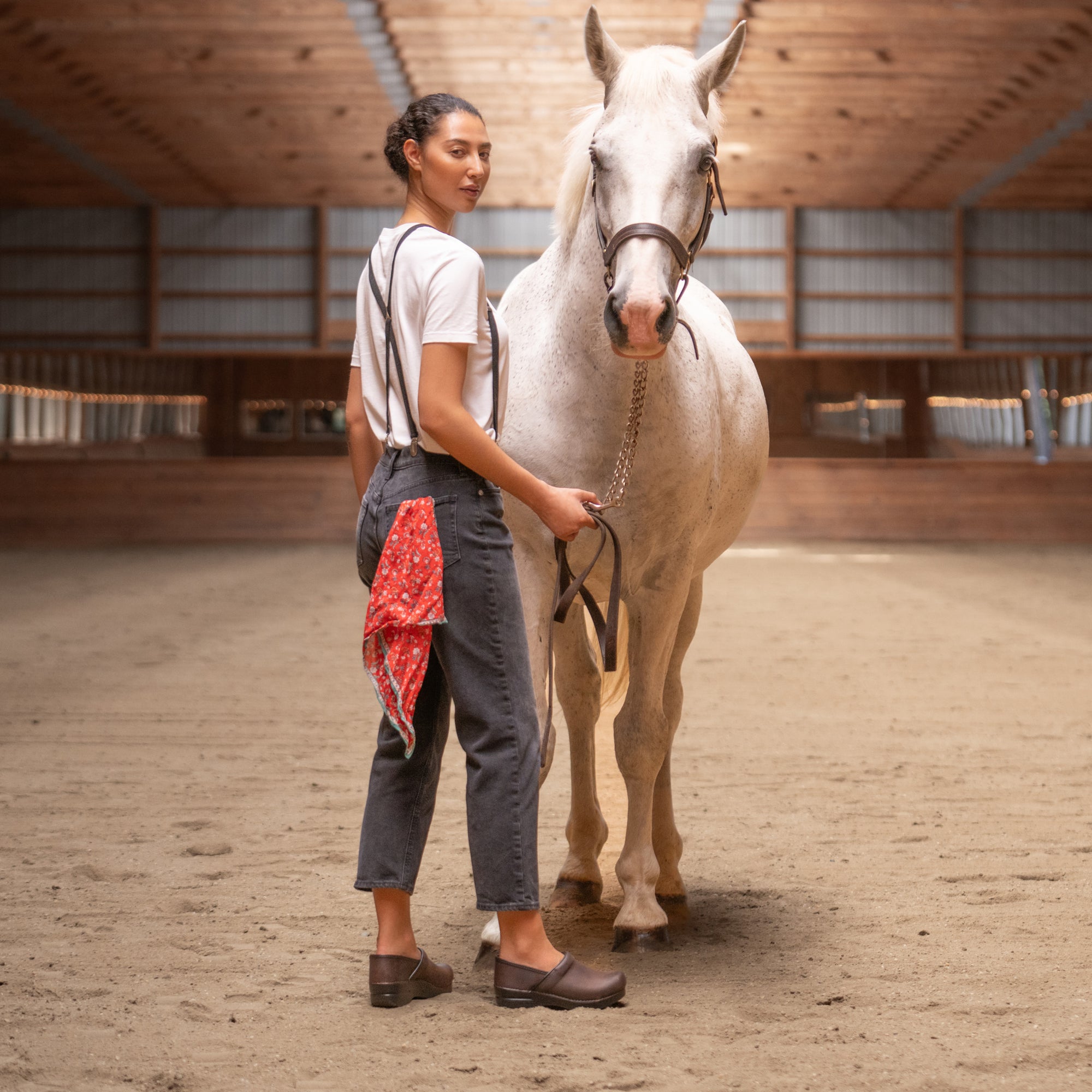 A woman working with a horse while wearing supportive brown clogs.