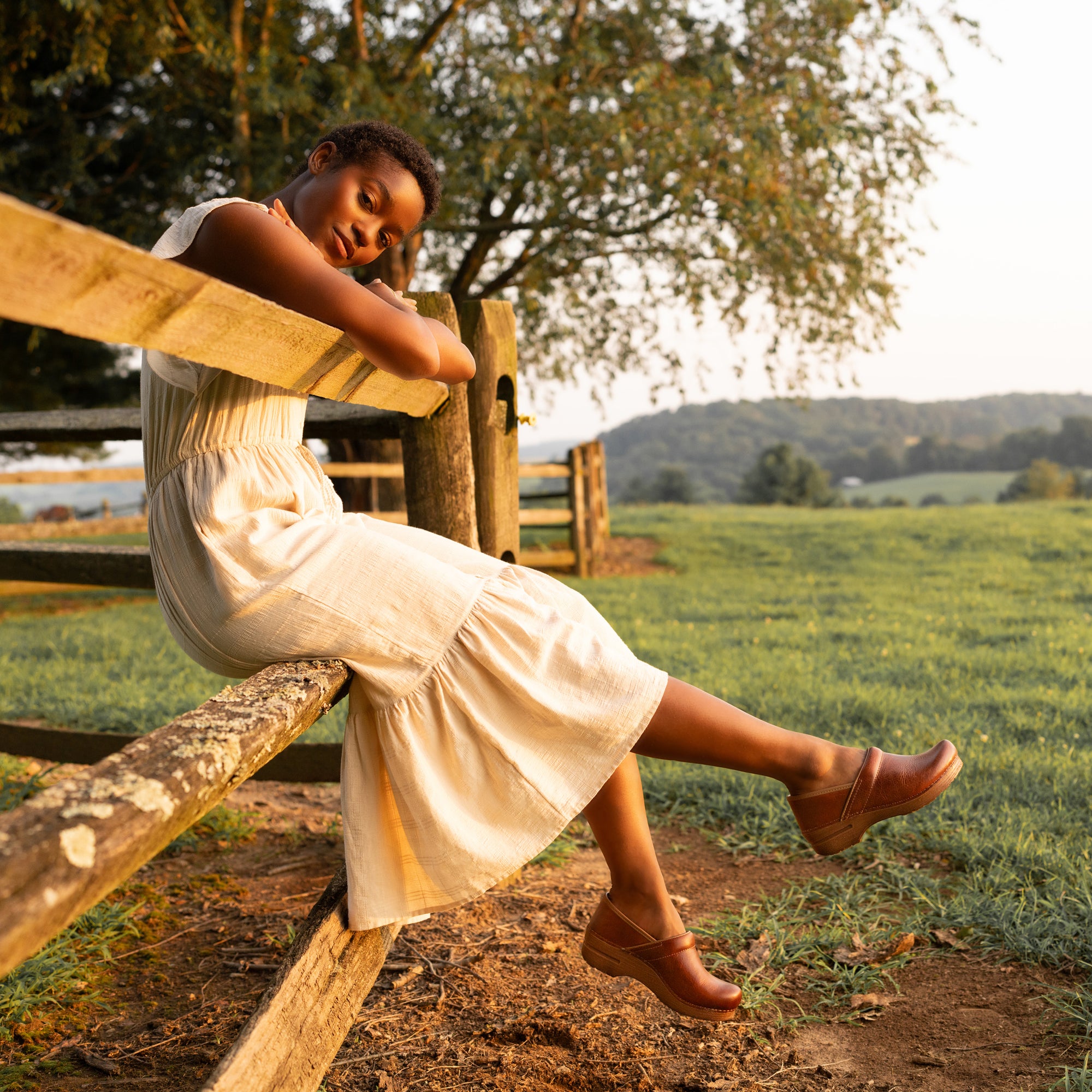 Woman in white dress and brown clogs in an open field.