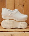 Traditional white clogs shown in front of a wood background.