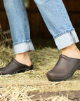 Brown backless clogs shown in a barn environment.