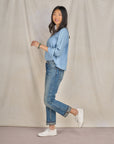 A woman in denim attire wearing casual white leather sneakers.