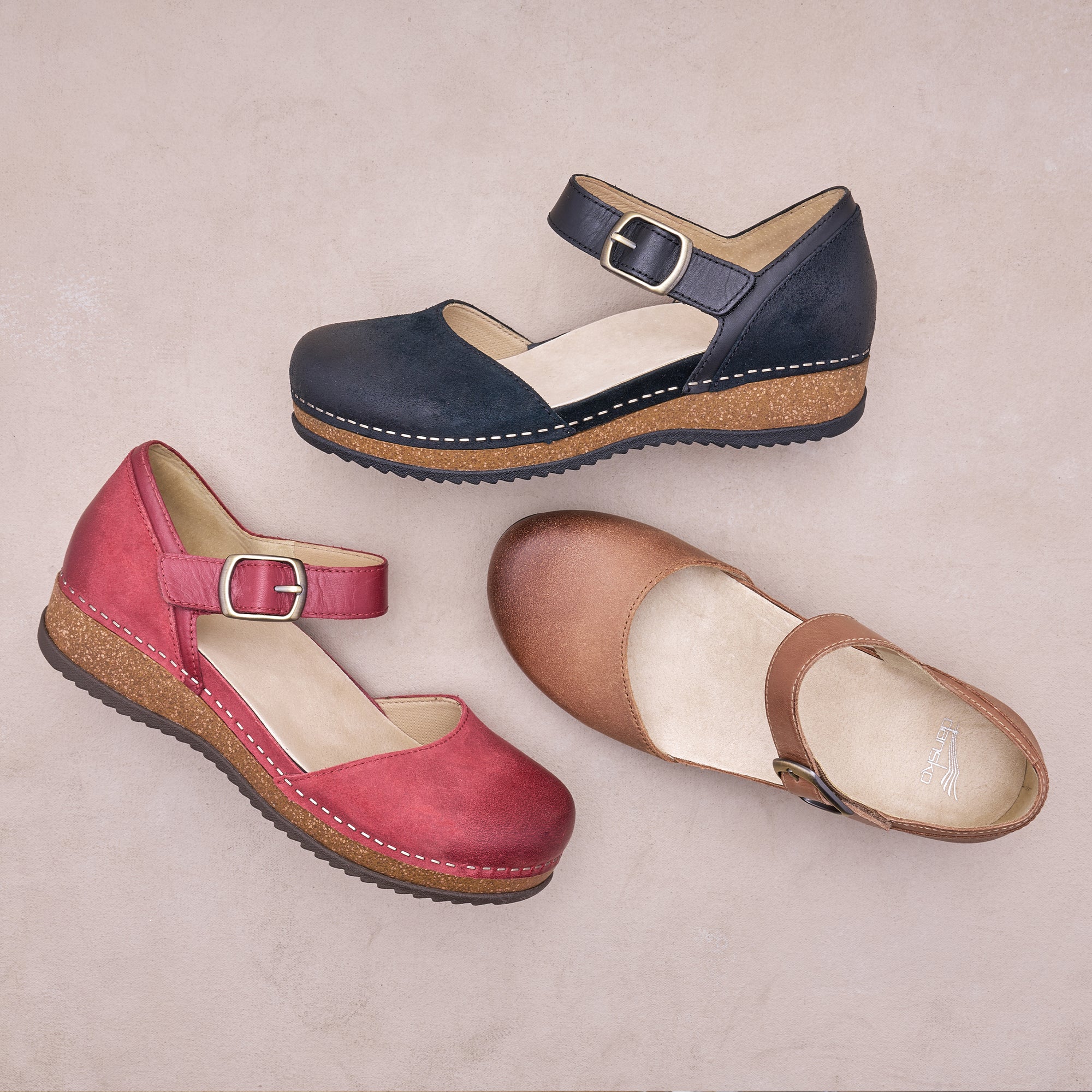 Flat lay with beige background. Three mary jane shoes in red, black and brown sit at different angles in the center of the image.