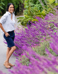 A woman standing amongst lavender flowers wearing tan clogs with a heel strap.
