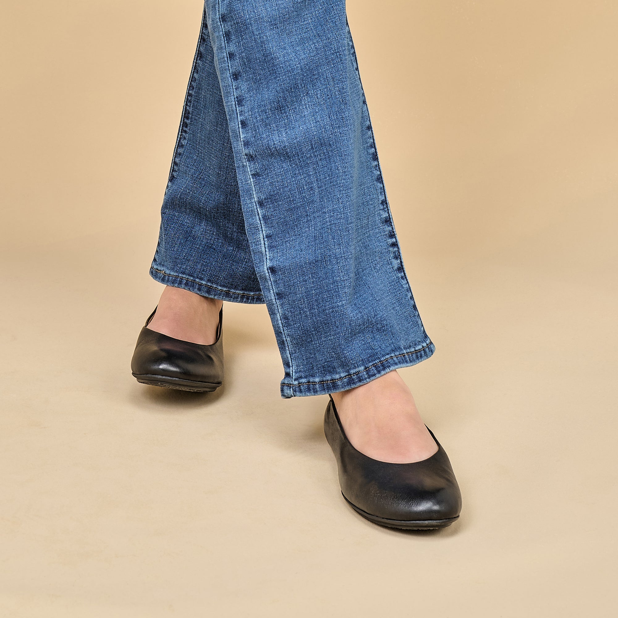 A closeup of black ballerina flats shown on foot.