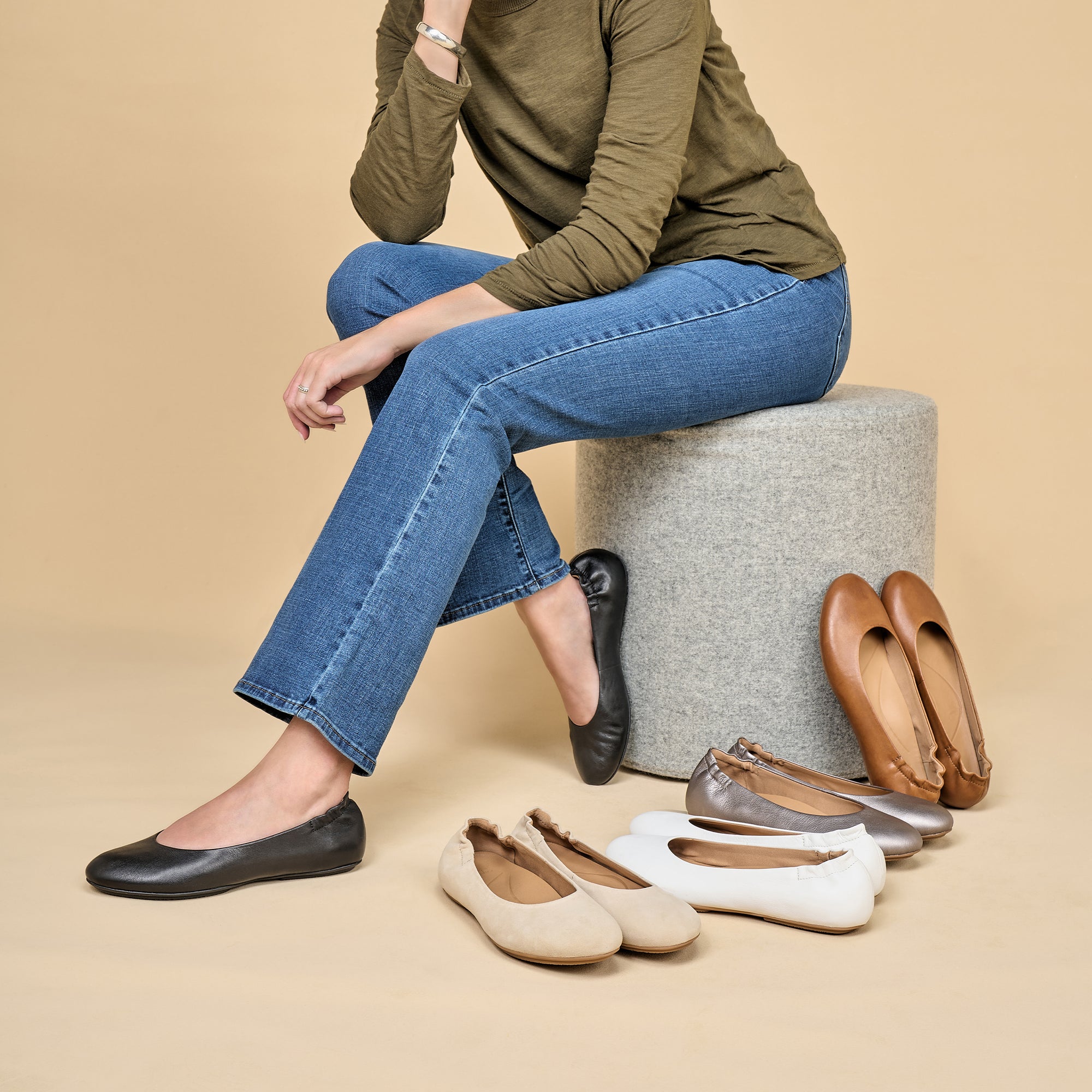 A woman wearing black ballerina flats with colors also shown in brown, silver, white, and tan.