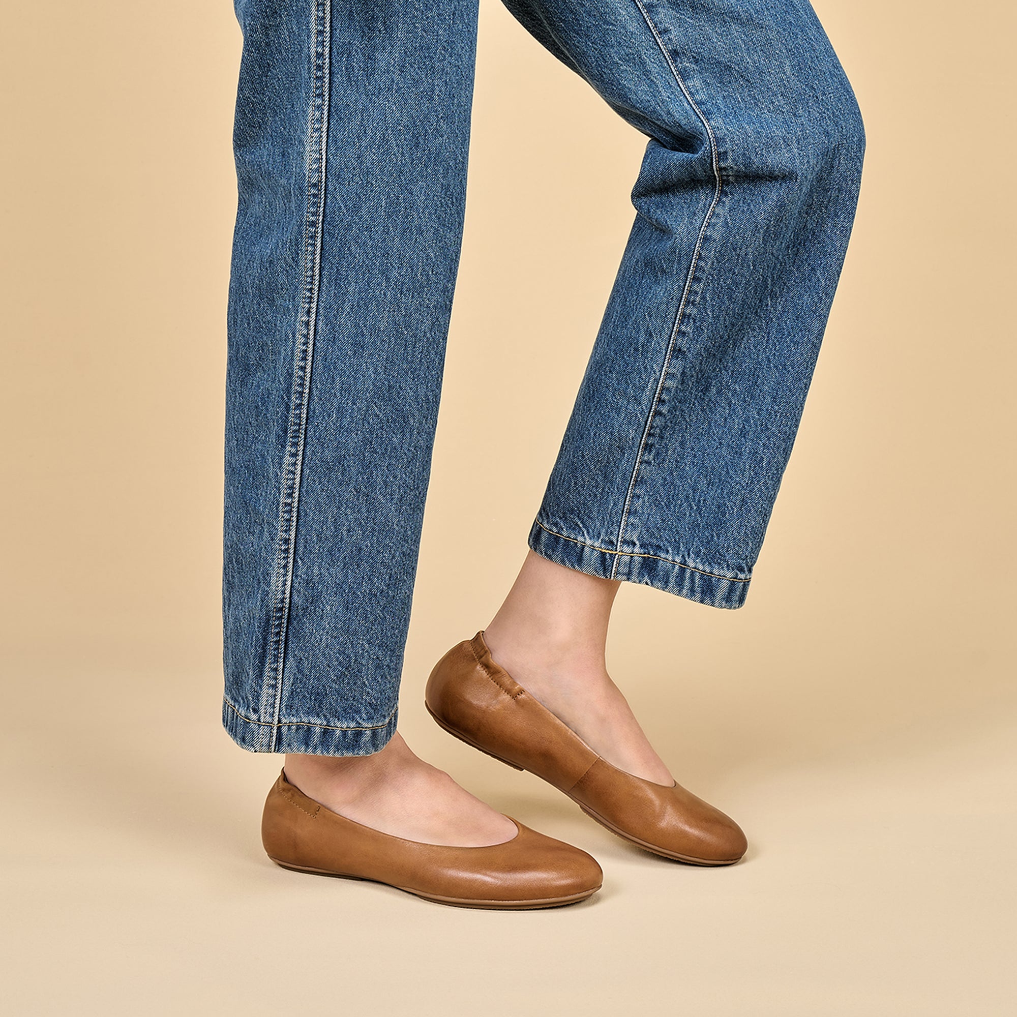 A closeup of brown ballerina flats shown on foot.