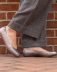 A closeup of metallic silver ballerina flats shown on foot.
