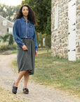 A woman in a plaid dress and denim jacket wearing black clogs with a buckle.
