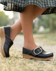 An on-foot shot of black clogs with a buckle that has "Est. 1990" detail.