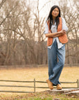Woman standing outdoors wearing a bright vest, blue button down, jeans, and honey platform Dansko clogs.