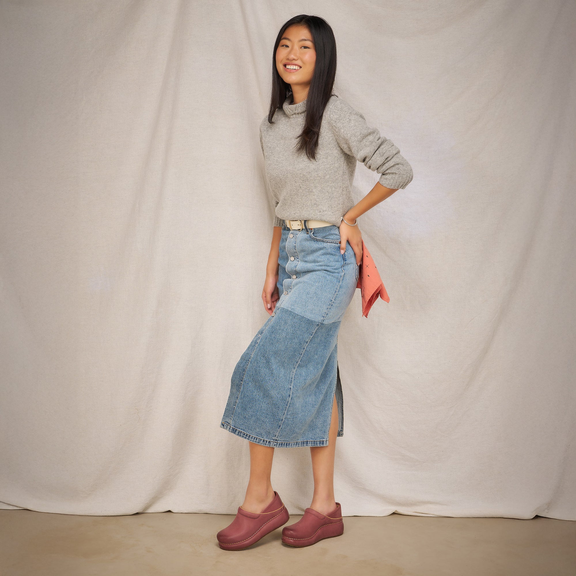 Woman in grey sweater, denim skirt and rose platform Dansko clogs.