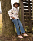 A woman on a farm in a quilted sweater wearing brightly neutral pink clogs.