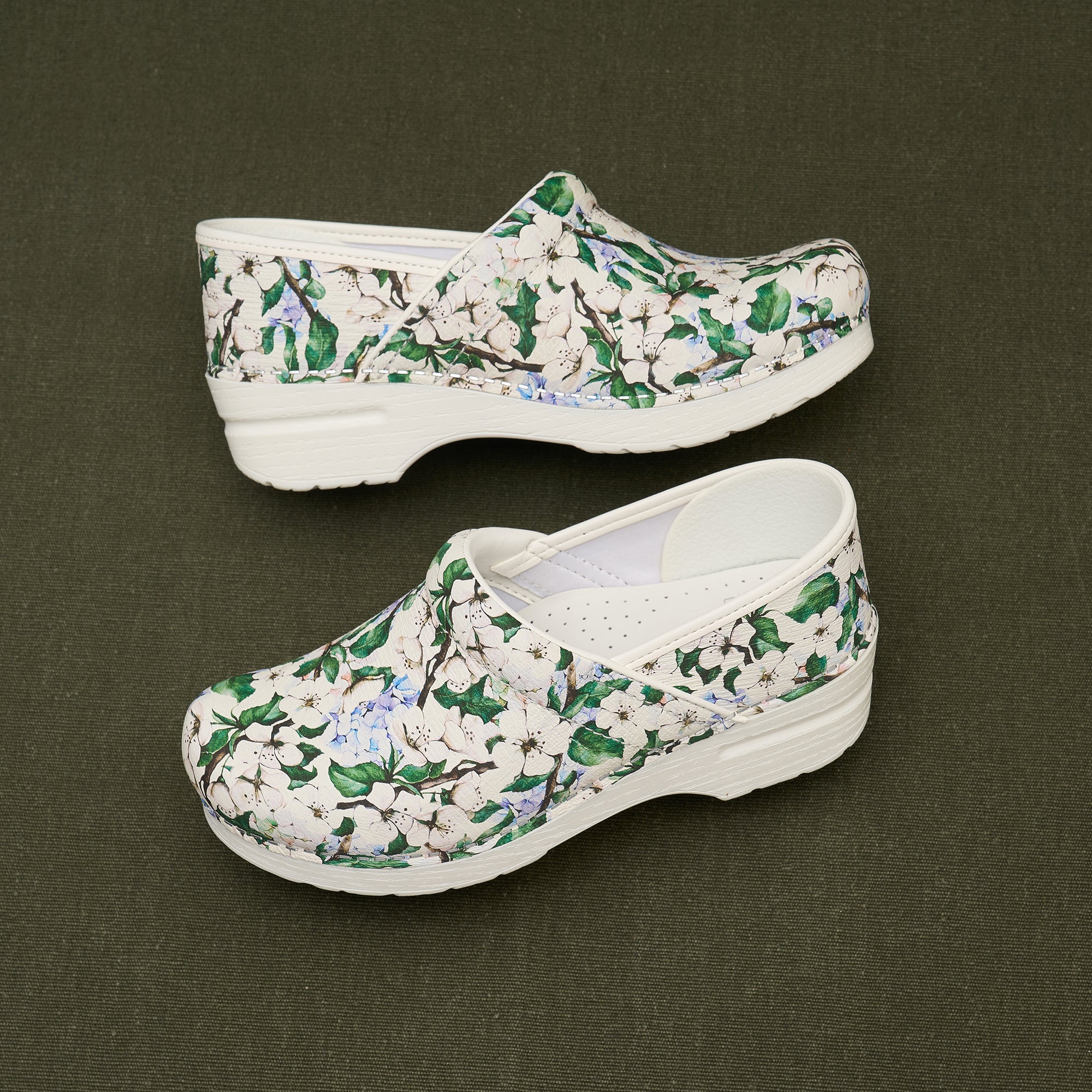 White clogs with a leaf and flower pattern shown against a dark background.