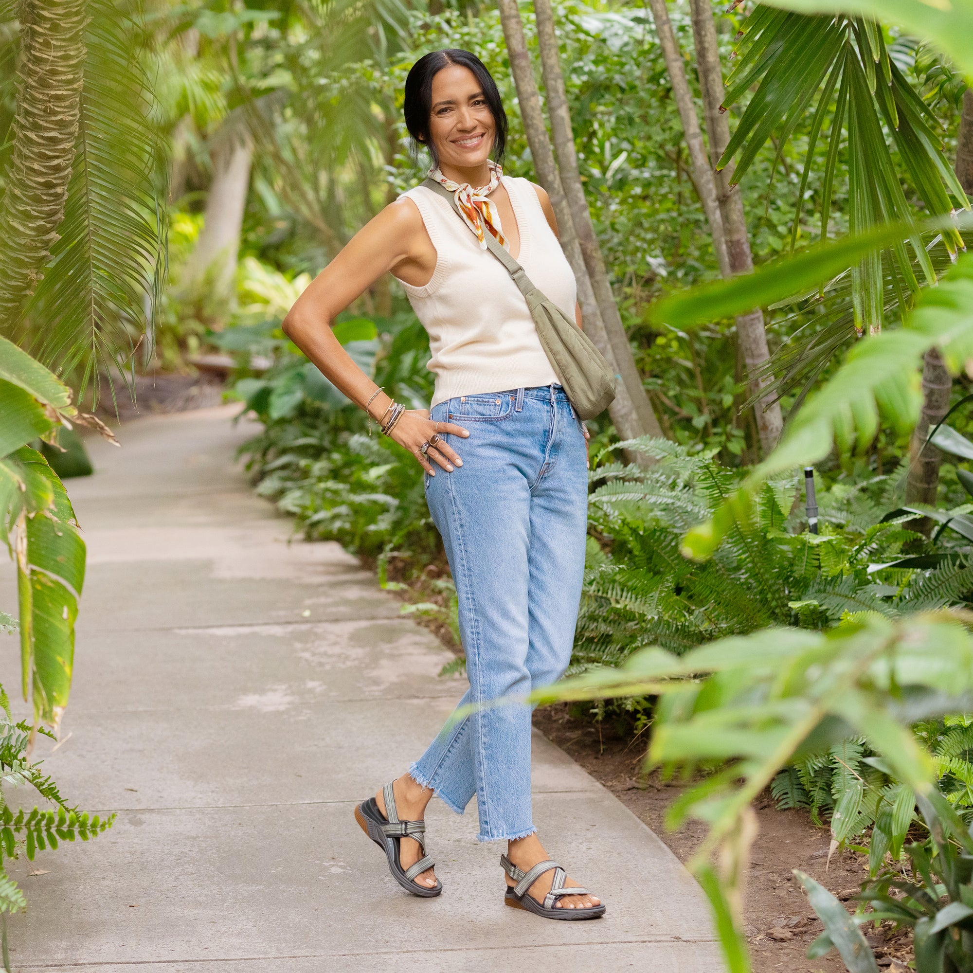 A woman standing on a nature path dressed casually while wearing strappy walking sandals.
