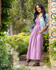 A woman standing in a garden wearing a purple dress and metallic leather flat sandals.