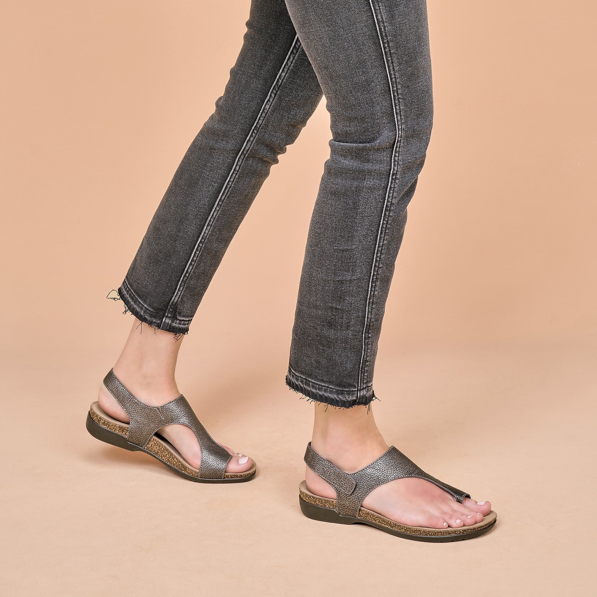 A closeup of metallic leather sandals worn with black jeans.