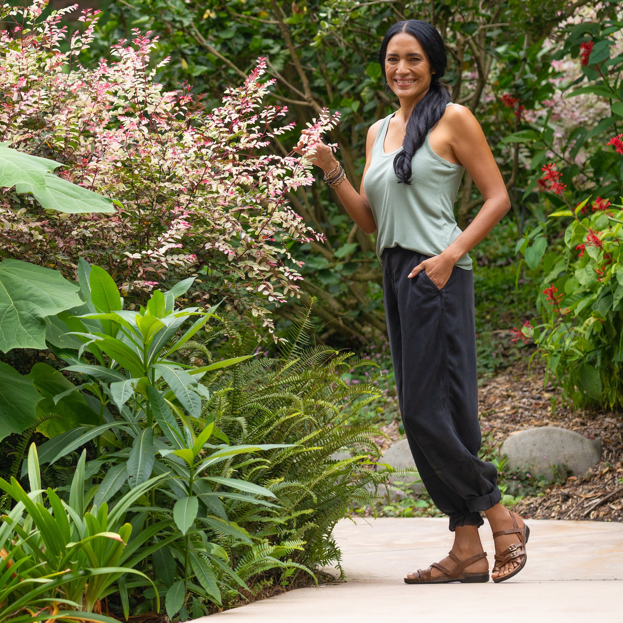 A woman standing on a garden path in a casual outfit wearing flat brown sandals.
