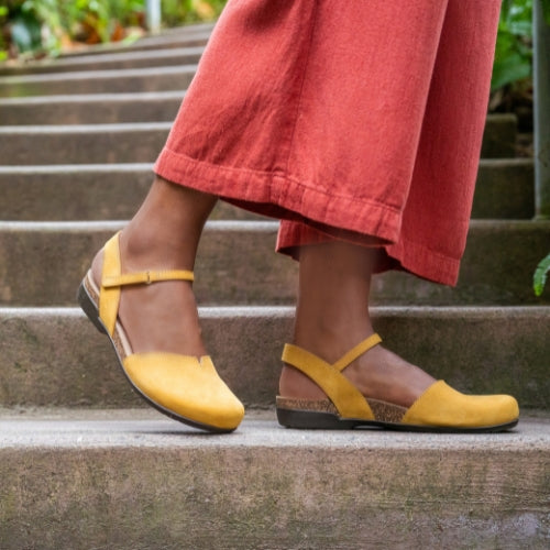 A close up of yellow sandals with a vamp & quarter silhouette and cork sole.