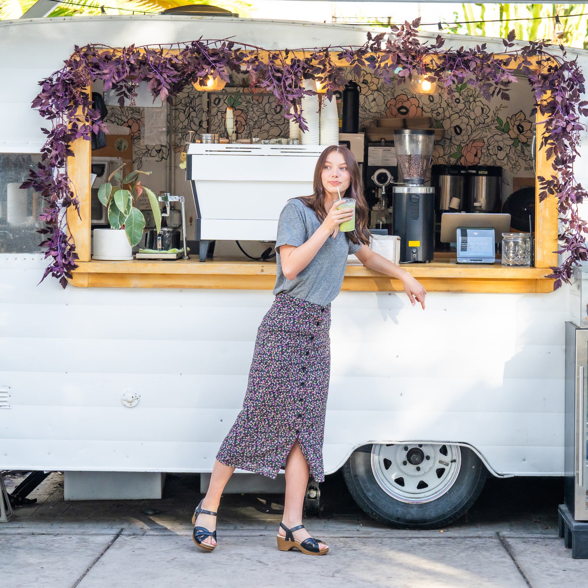 A woman ordering a drink and wearing a casual outfit stands on black flatform sandals with a unique strap design.