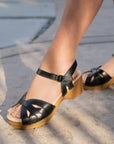 A closeup of black leather open-toe sandals with an adjustable ankle strap.