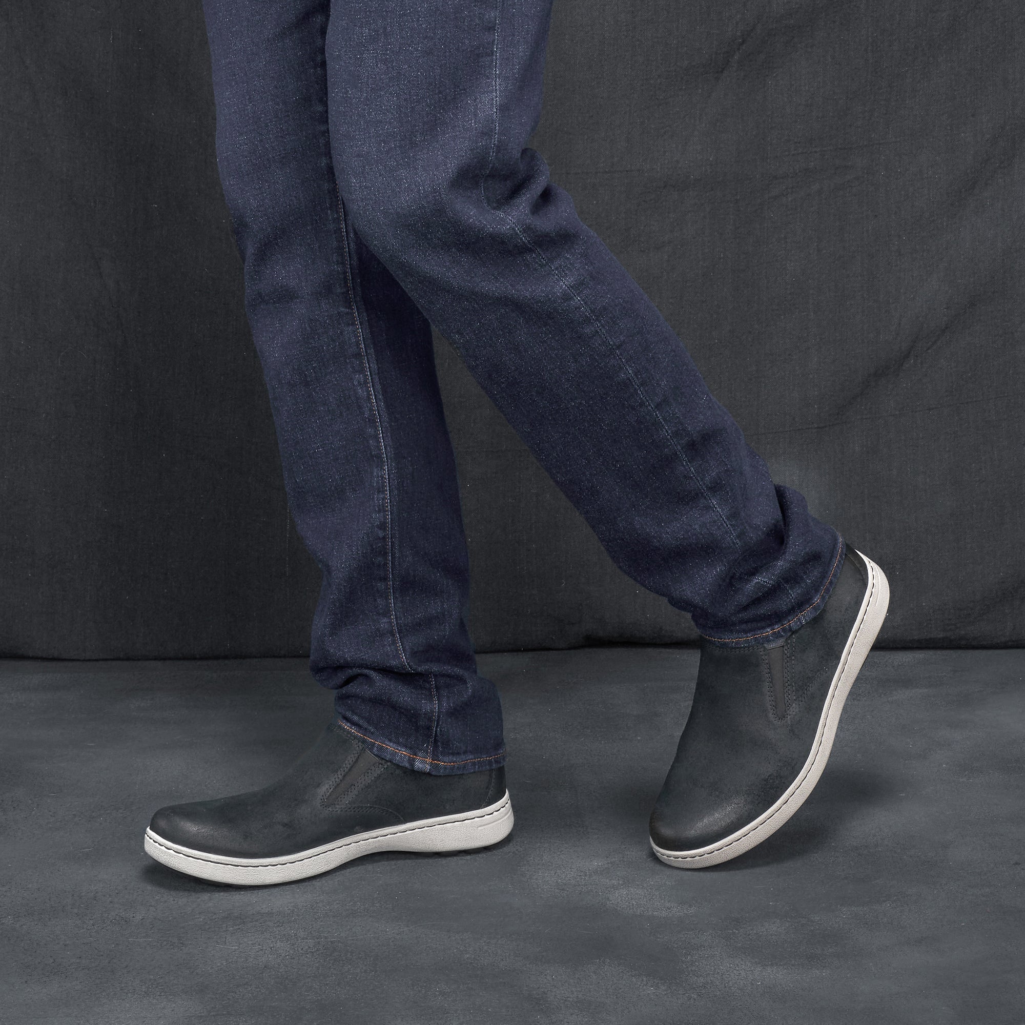 Man in jeans wearing black leather slip-on sneakers.