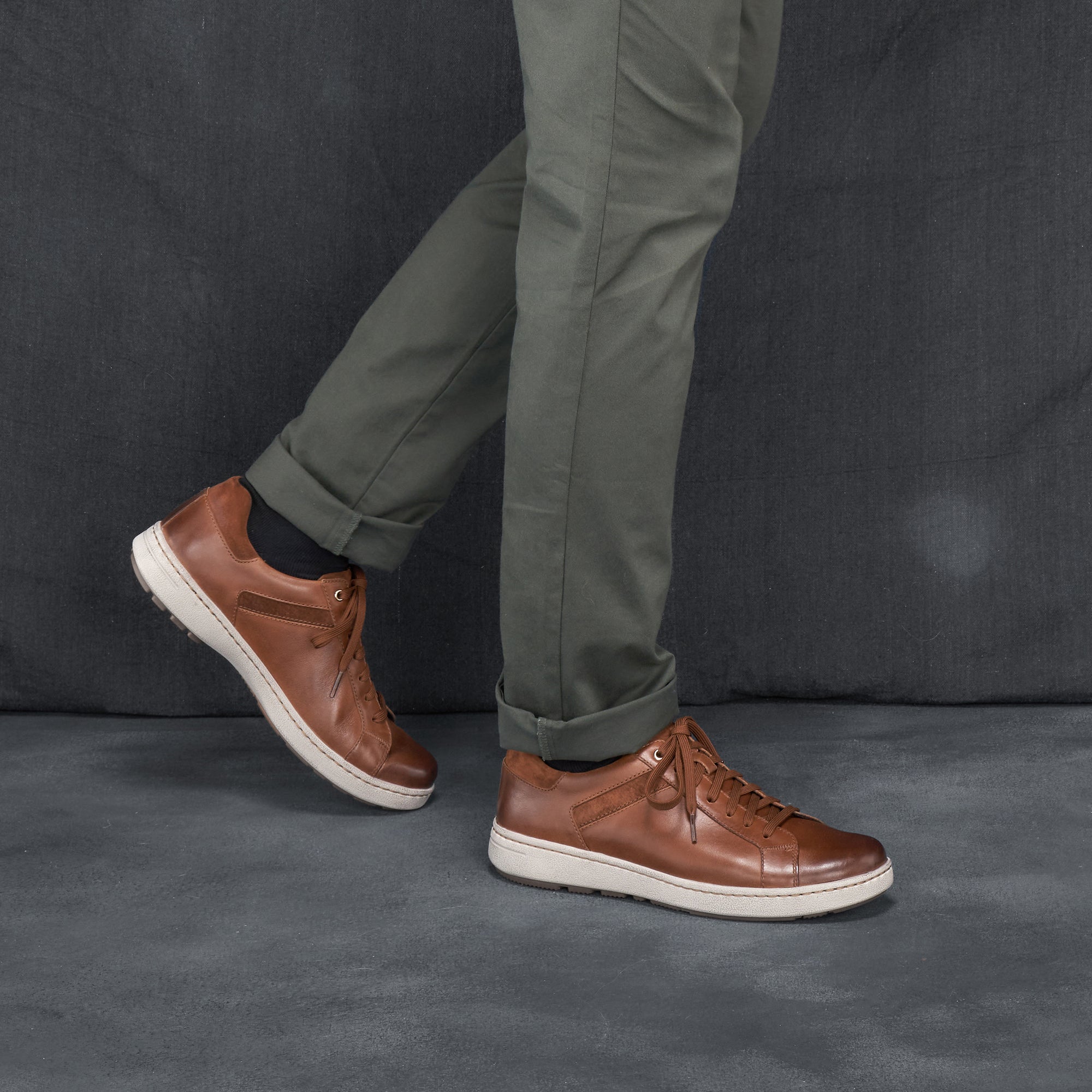 Man in grey chinos wearing trendy and stylish brown leather sneakers.