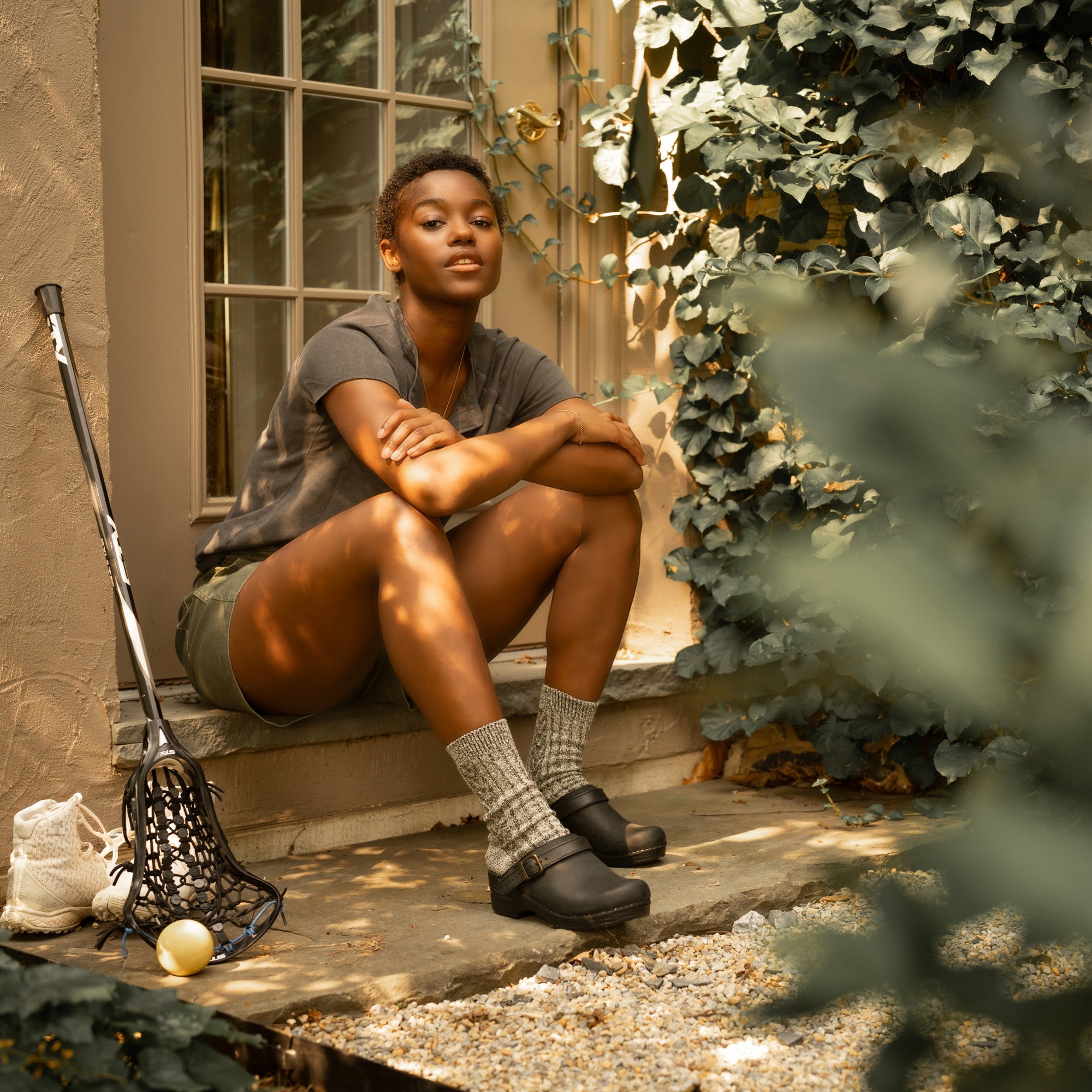 A woman sitting on a stoop and wearing black swivel strap clogs with grey wool socks.