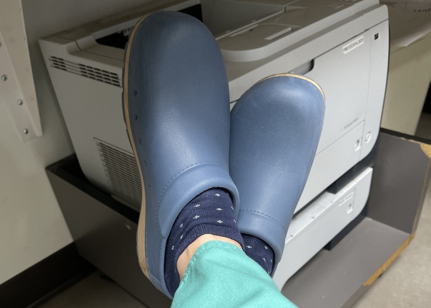 User generated content of healthcare professional with feet kicked up in blue molded mules.