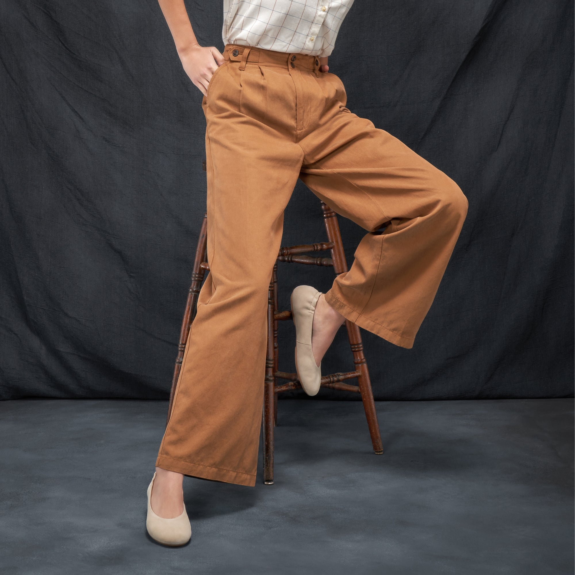 A woman seated casually in tan pants wearing tan leather flats.