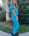 A nurse wearing blue scrubs and black clogs with personalized initials.