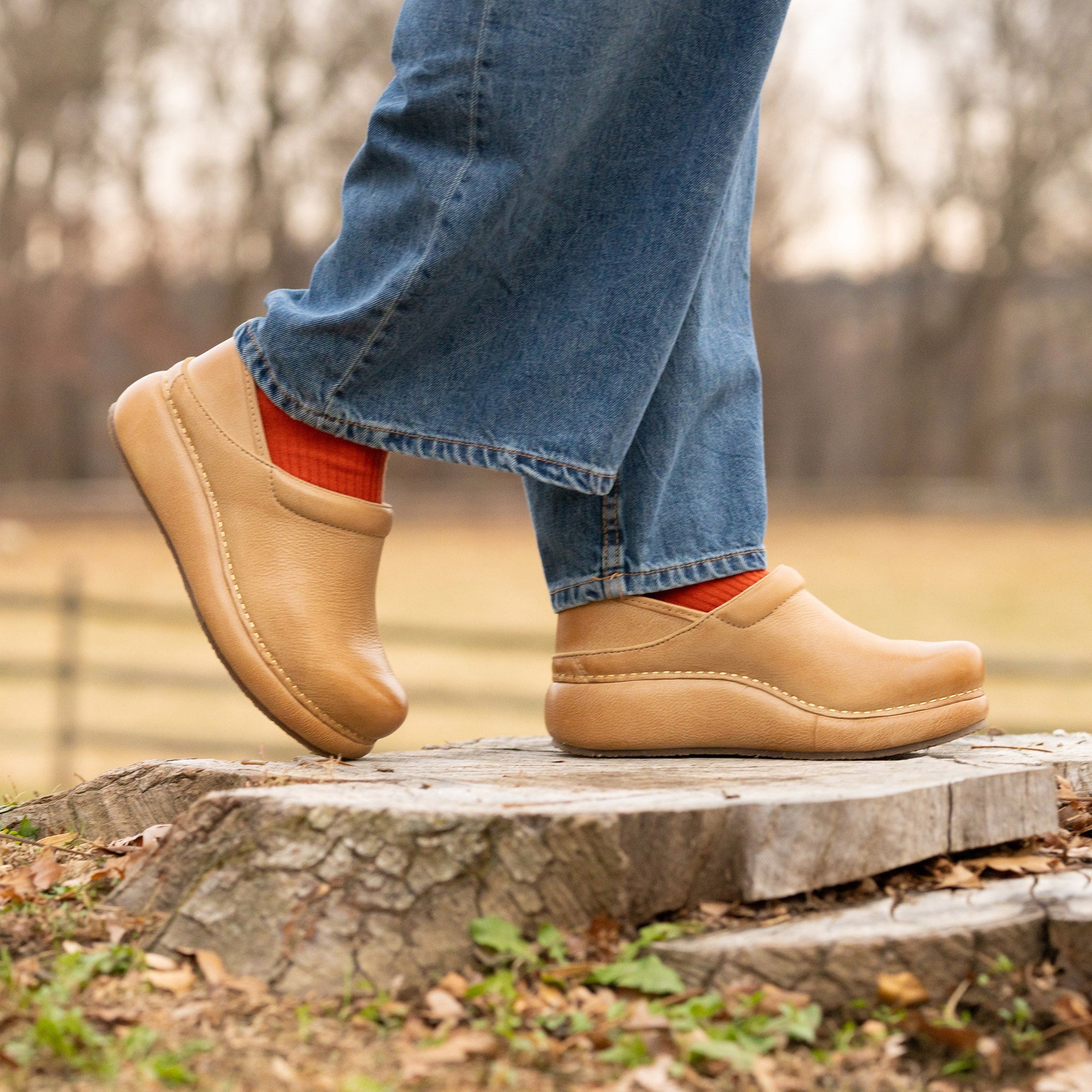 Blue mules with stripe socks on a model wearing dark pants. Dark backdrop.