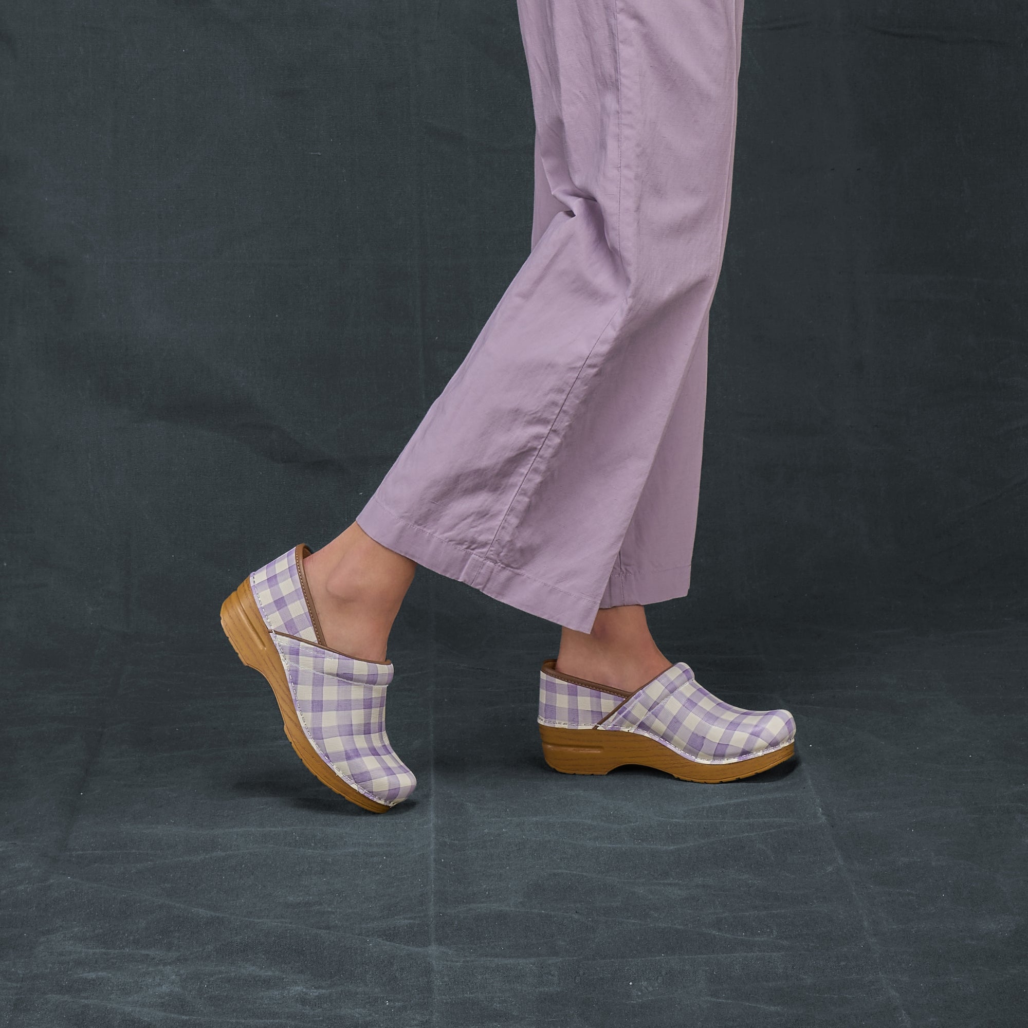 A close look at the lavender plaid clogs against a dark background.