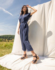 Woman in field in front of neutral backdrop wearing a jumpsuit and black mary jane heels with wood bottoms.