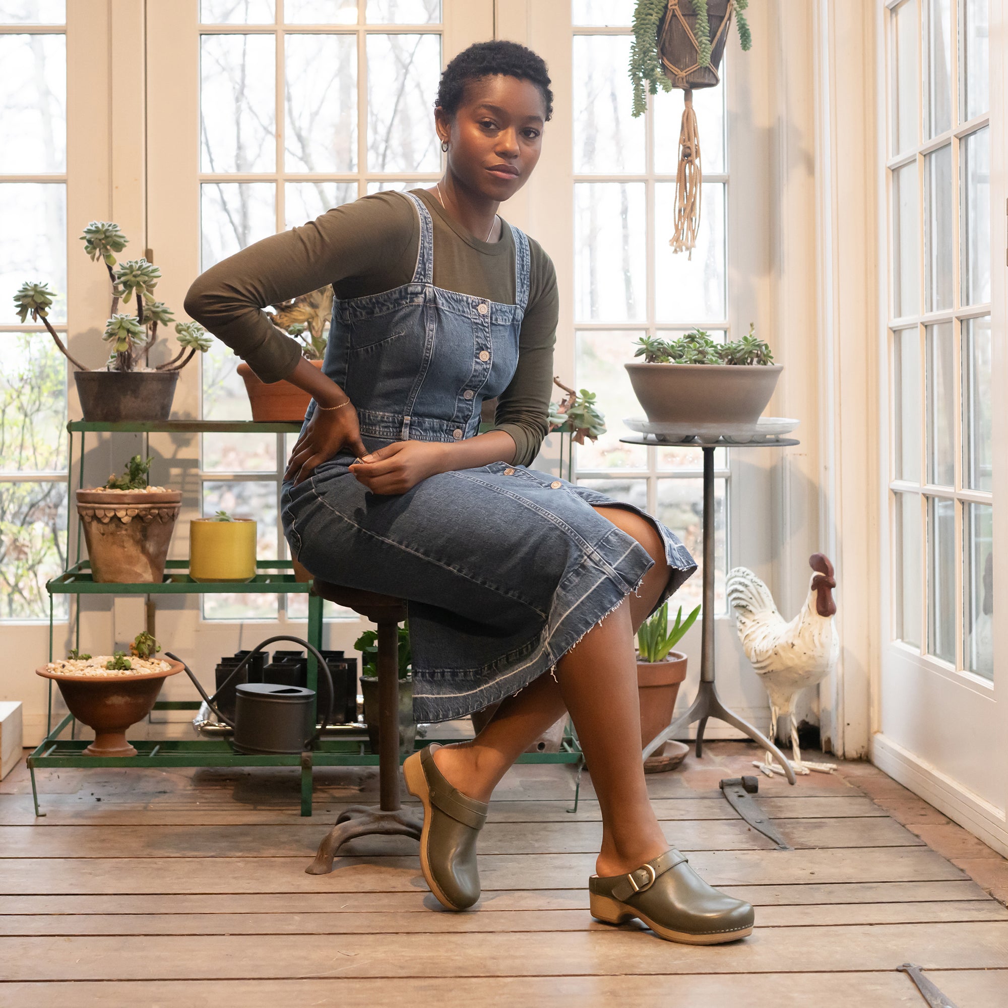 A craftswoman in her studio wearing a denim dress and forest green mule clogs.