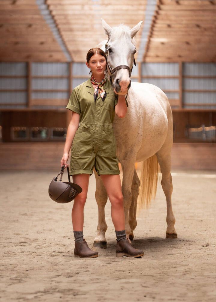 A woman in a green jumpsuit and durable brown clogs while helping to train a horse.