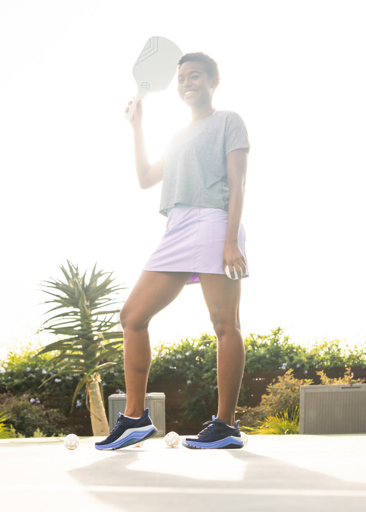 A woman with a pickleball paddle in a casual athletic outfit and navy-blue performance athletic sneakers.