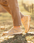 A closeup of compact, lightweight sneakers in a neutral tan shown on foot.