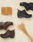 A brown pair of boots and a black pair of boots shown with barn materials.