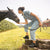 A farmgirl in denim coveralls wearing black boots while working with horses.