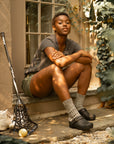 A woman sitting while wearing black backless clogs and casual clothes.