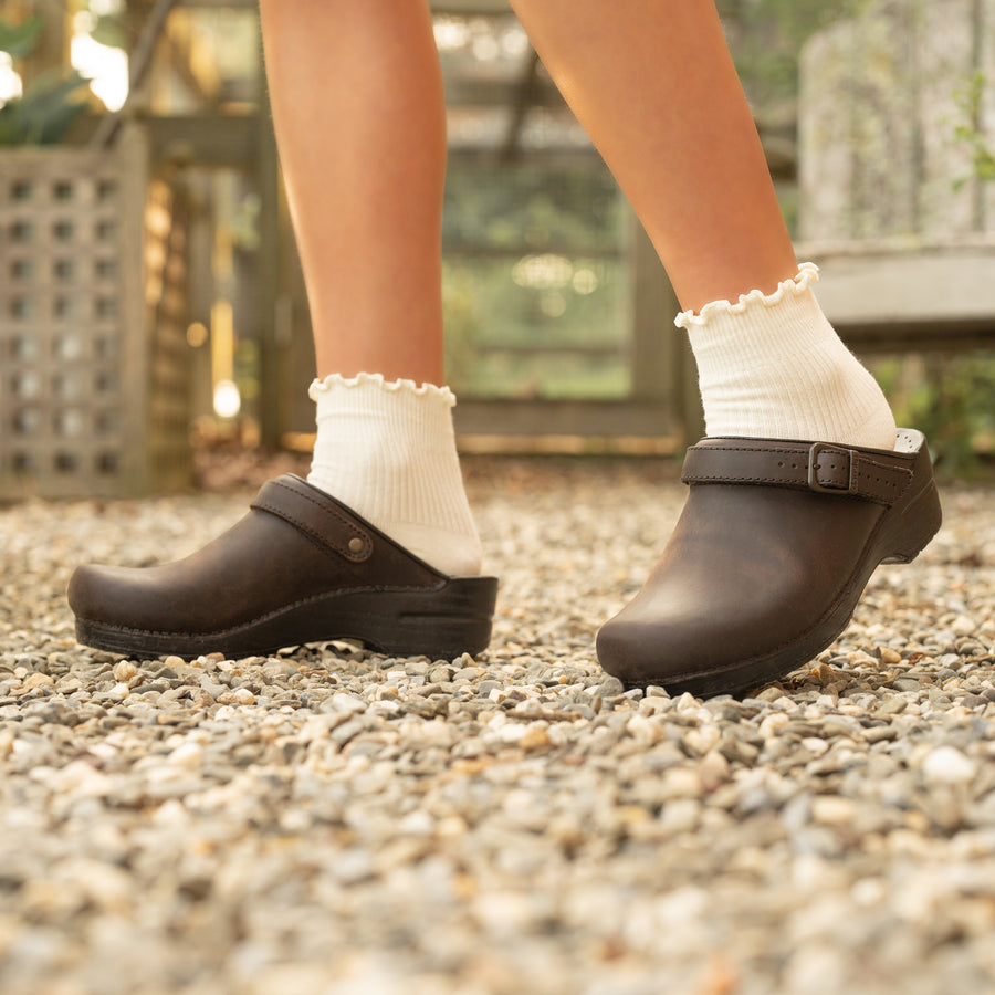 Brown backless clogs with an adjustable swivel strap styled with scalloped white socks.