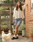 Brown mule clogs with an adjustable strap styled with a flowy white shirt and denim shorts.