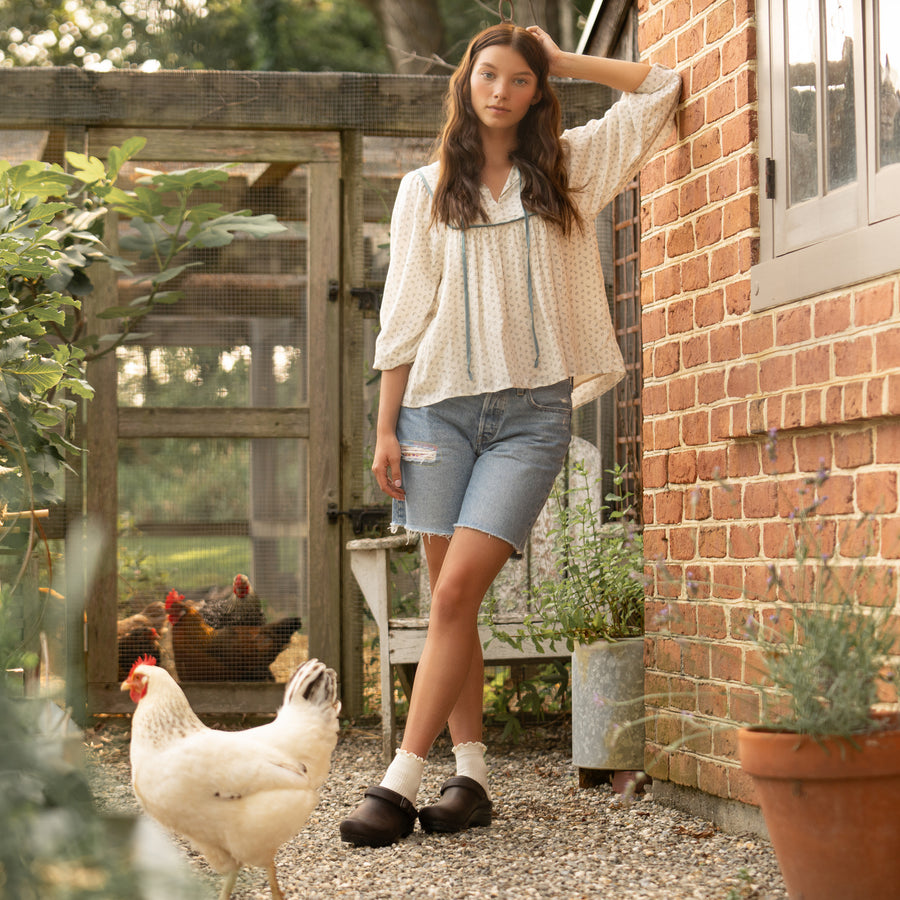 Brown mule clogs with an adjustable strap styled with a flowy white shirt and denim shorts.