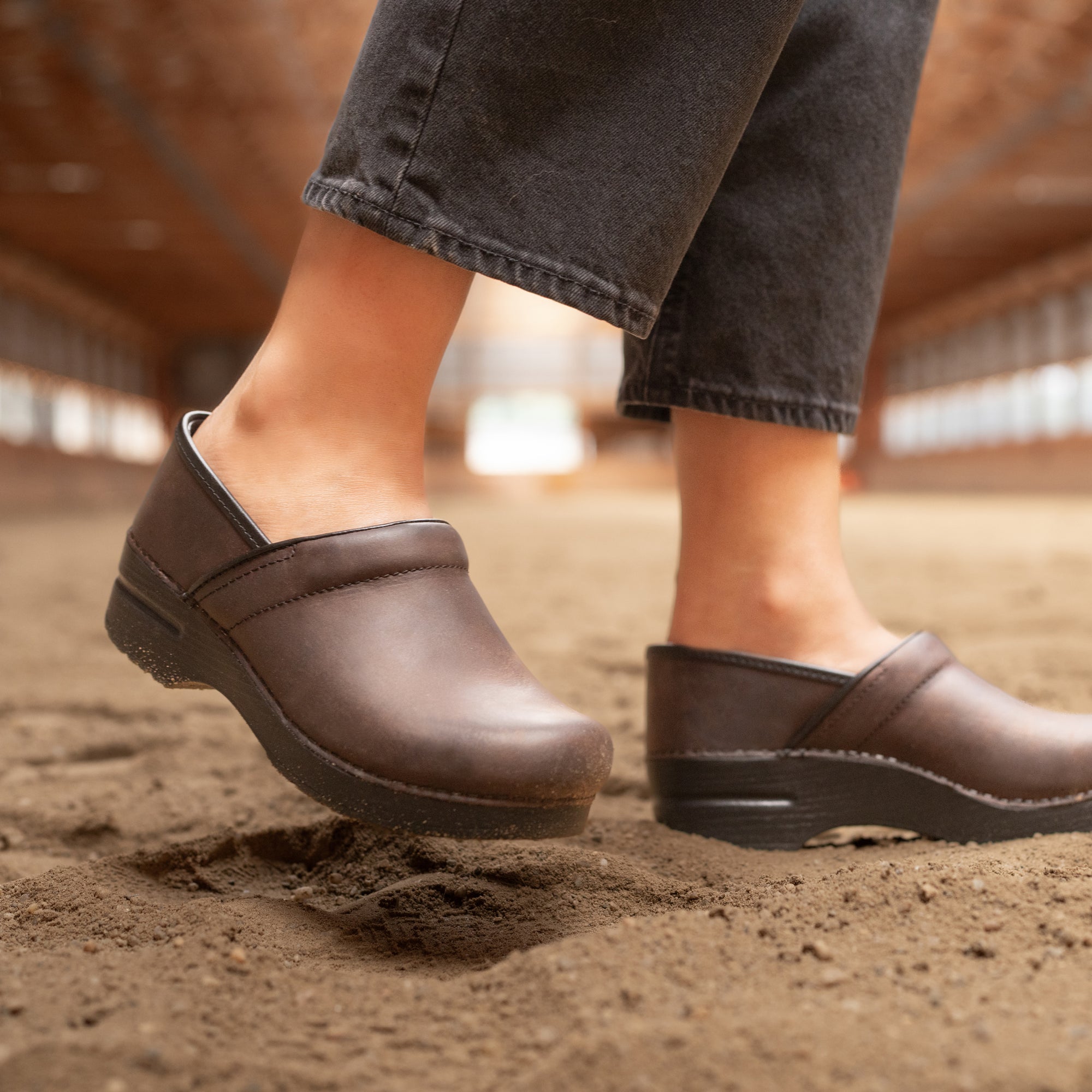 Brown Professional clogs shown with black jeans in a barn setting.